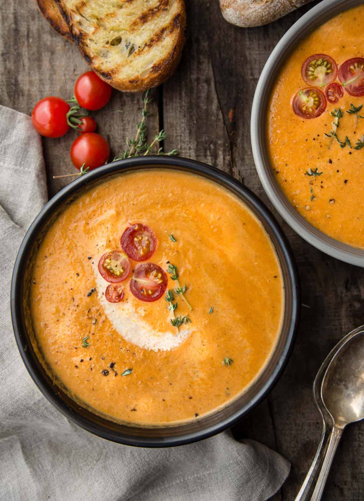 A bowl of smoked tomato bisque topped with fresh tomatoes and a side of toasted bread