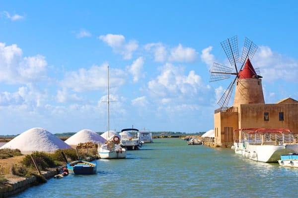 A Sicilian salt mine along a canal showing large mounds of sea salt.