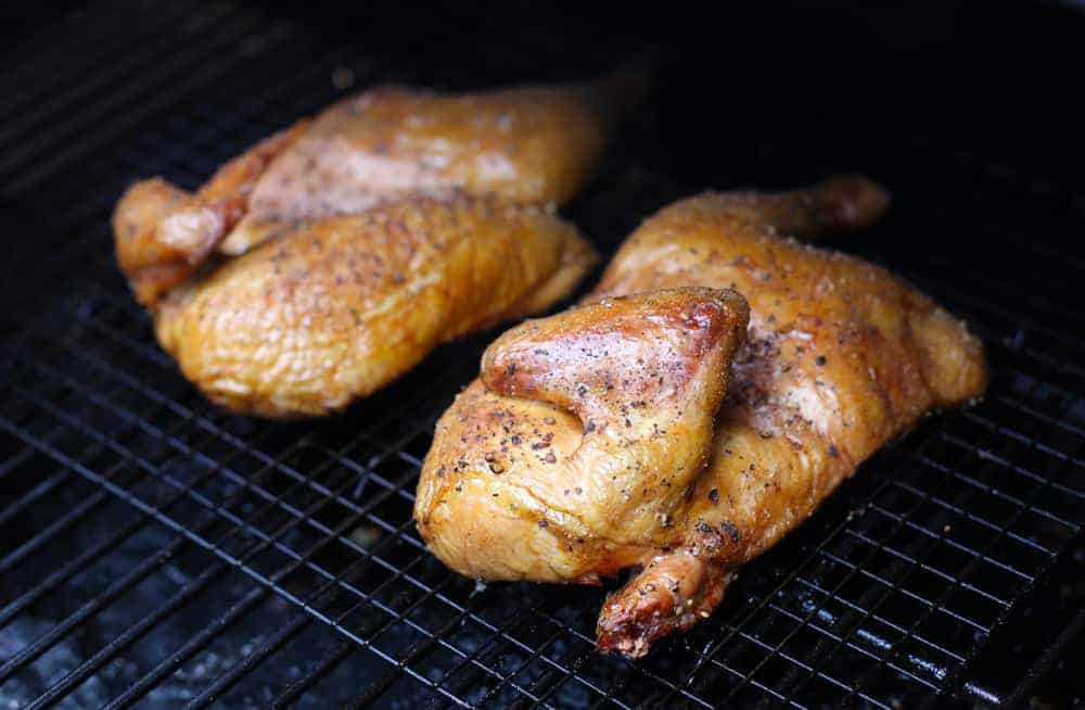 Two chicken halves cooking on a smoker