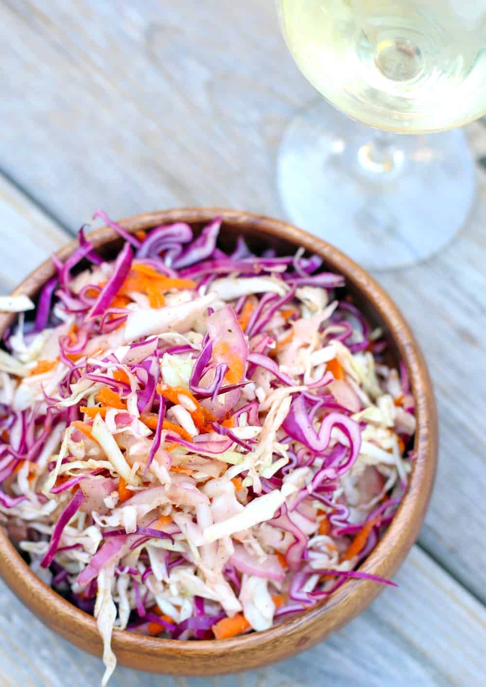 Easy Mayo-Free Coleslaw in a bowl with a glass of wine