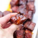 A hand holding a single Pork Belly Burnt Ends