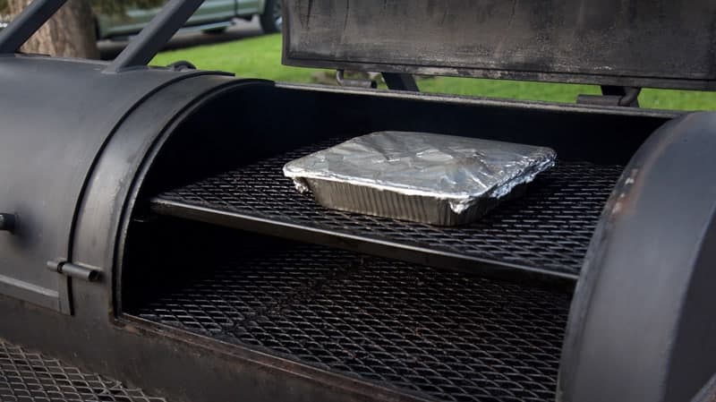 Meat in a covered aluminum tray on a smoker
