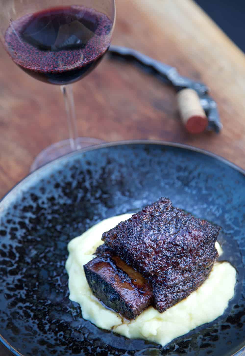 A plate of beef with mashed potatoes and a glass of wine