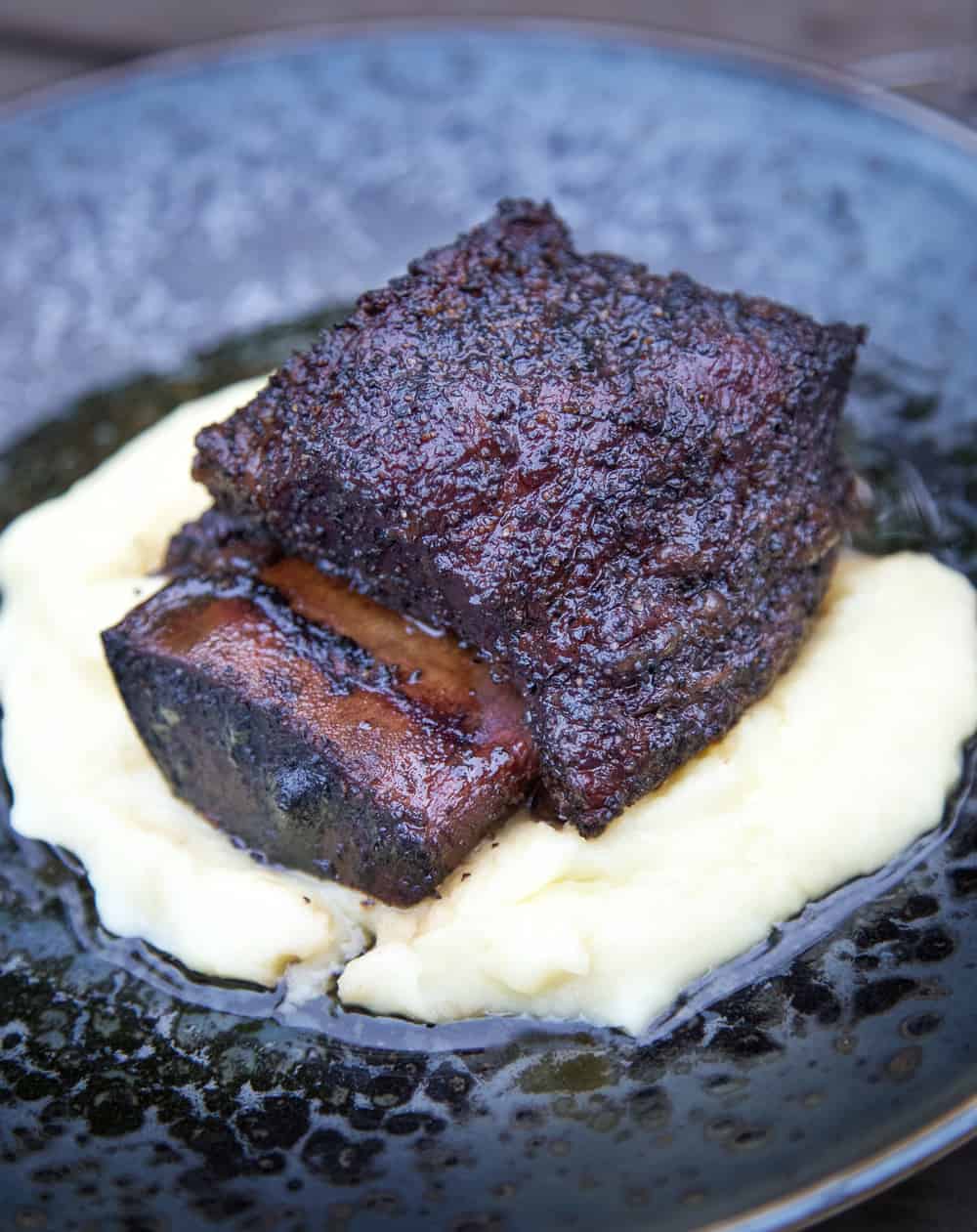 Recipe for smoked beef short ribs and tips and tricks for getting that melt-in-your-mouth tender meat. Smoked Beef Short Ribs on a plate with mashed potatoes