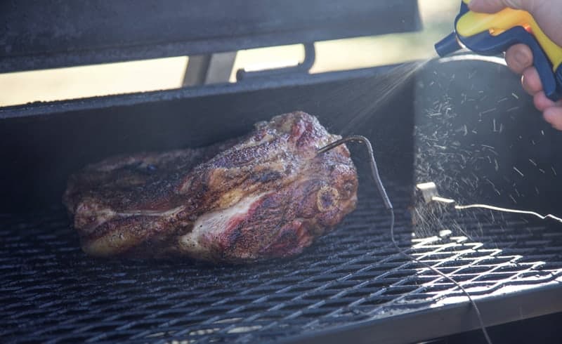 Spritzing the lamb shoulder on the smoker