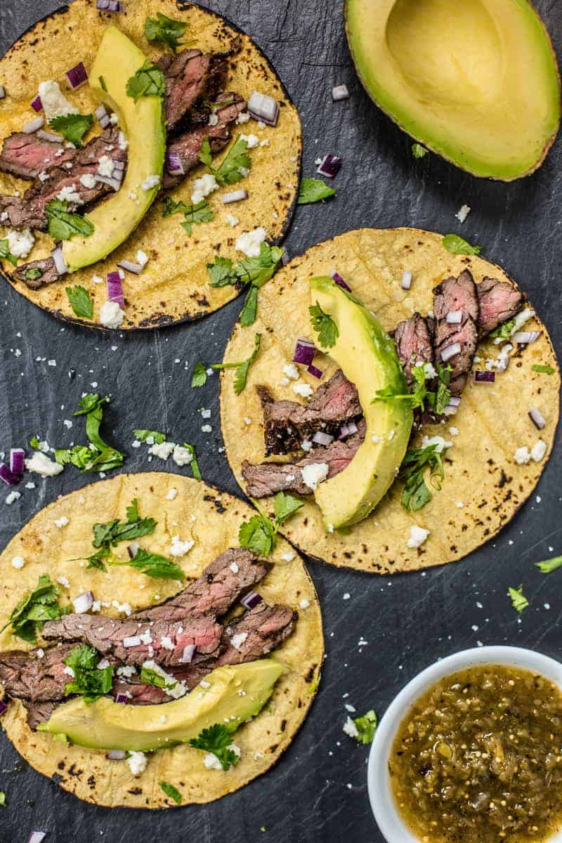Grilled Steak Tacos garnished with avocado, cilantro, and red onions