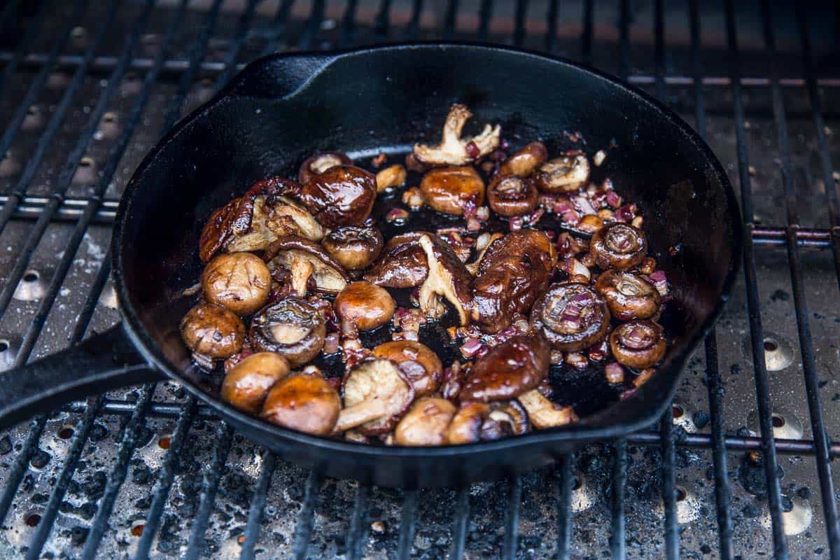 Mushrooms cooking in a cast iron pan on a grill.