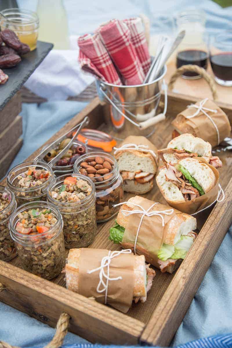 A picnic spread with cold lentil salad in mason jars and pork tenderloin sandwiches