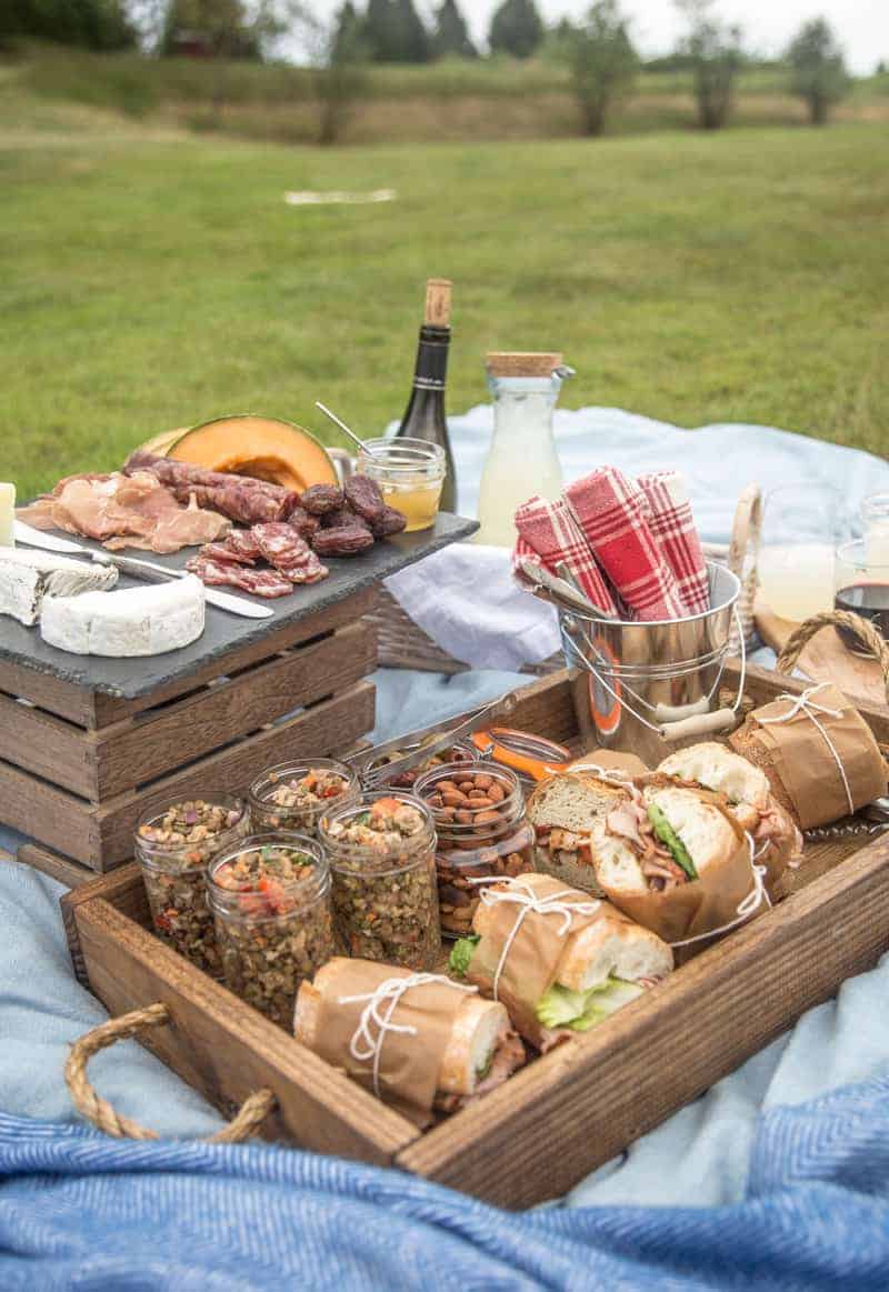 A picnic spread on a blanket with pork tenderloin sandwiches and a cold lentil salad.