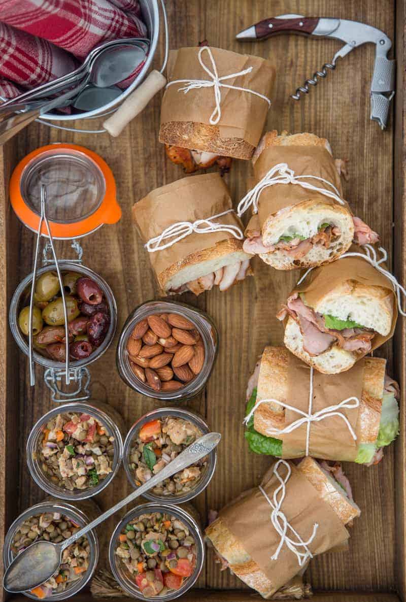 A picnic platter full of pork tenderloin sandwiches, almonds, lentil salad, and olives.