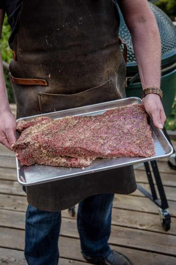 Seasoned raw and trimmed brisket on a sheet pan going on the smoker.