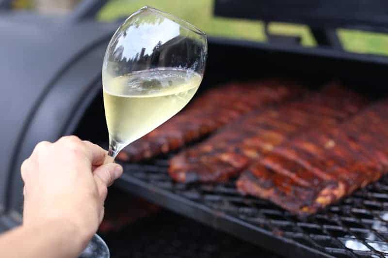 A glass of sparkling wine with three racks of smoked ribs