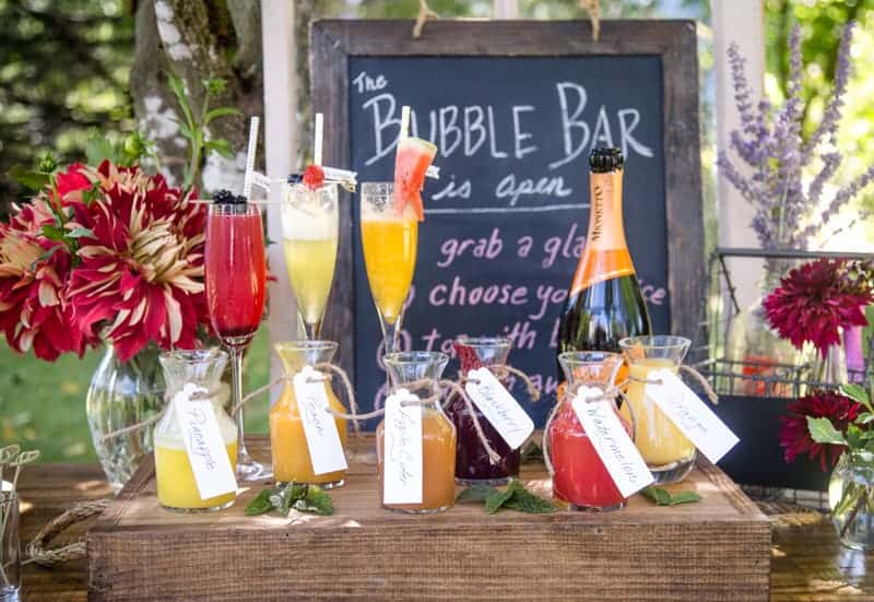 A table loaded with decorations and juices for a Mimosa Bar with bubbly, juices and garnish