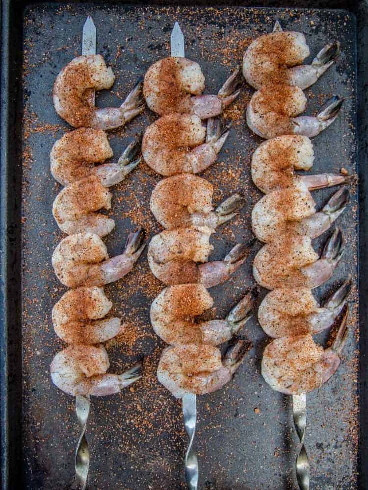 Seasoned shrimp on a grill skewer on a sheet pan before grilling.