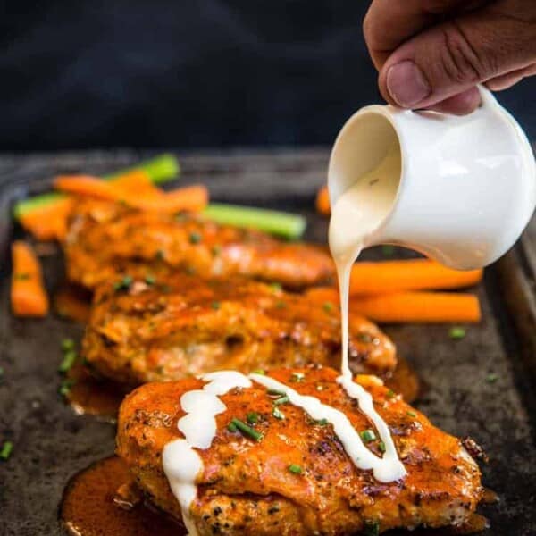 Buffalo stuffed chicken breasts on a platter with ranch being drizzled over the top.