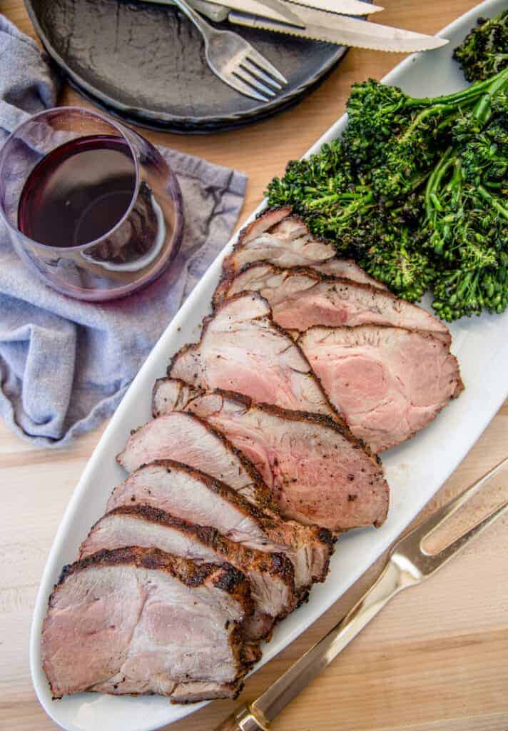 Grilled pork collar cut into slices with grilled broccolini and a glass of red wine