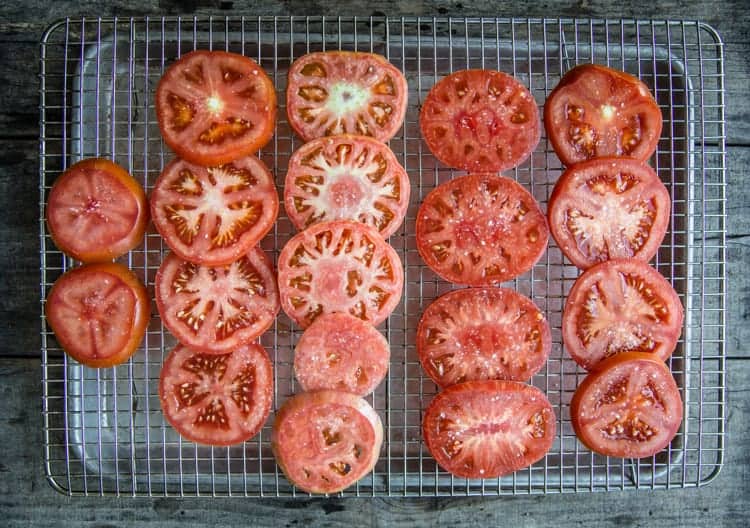 Raw sliced tomatoes salted on a cookie sheet.
