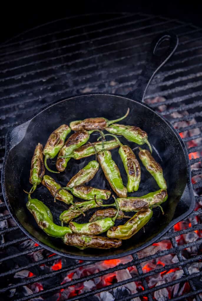 Shishito peppers being blistered in a cast iron pan on the grill