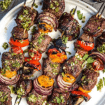 grilled steak and veggie skewers with a jalapeno parsley chimichurri sauce on a white plate, pin image