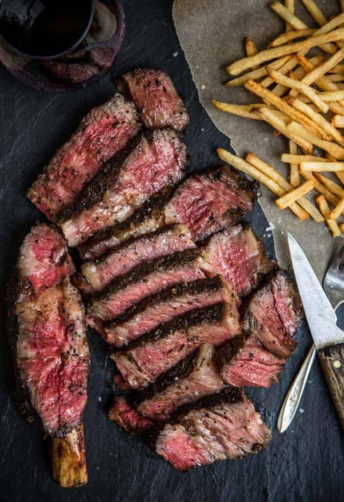 Reverse Seared Cowboy Ribeye sliced into thin strips with french fries and wine