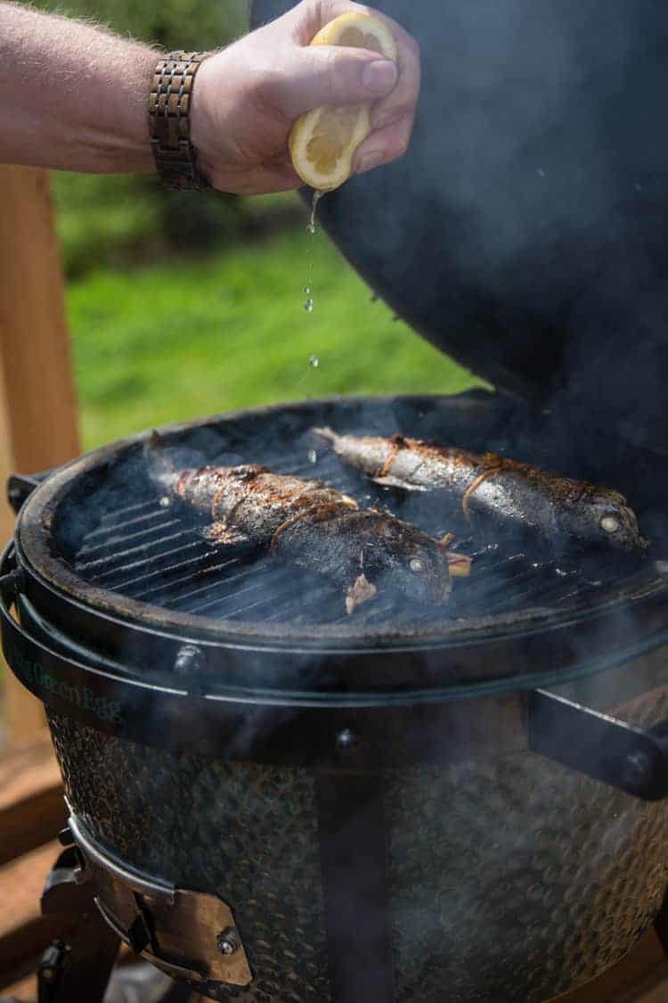 two whole fish on a big green egg being drizzled with lemon juice