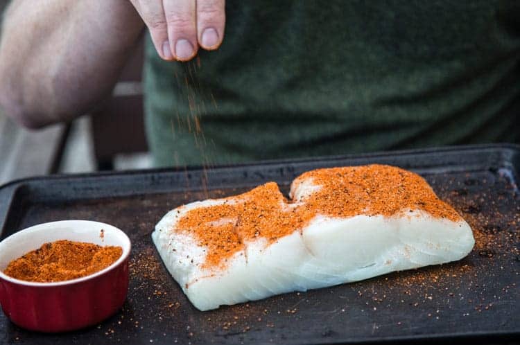 A large piece of white fish being sprinkled with homemade seafood seasoning