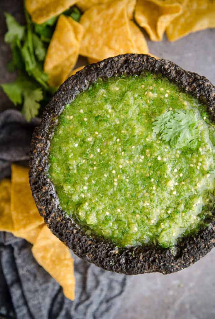 tomatillo salsa in a black bowl surrounded by chips