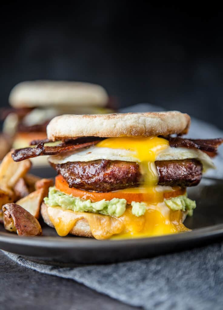 A Breakfast Sandwich topped with Smoked Sausage, an over easy egg, and smoked bacon. 