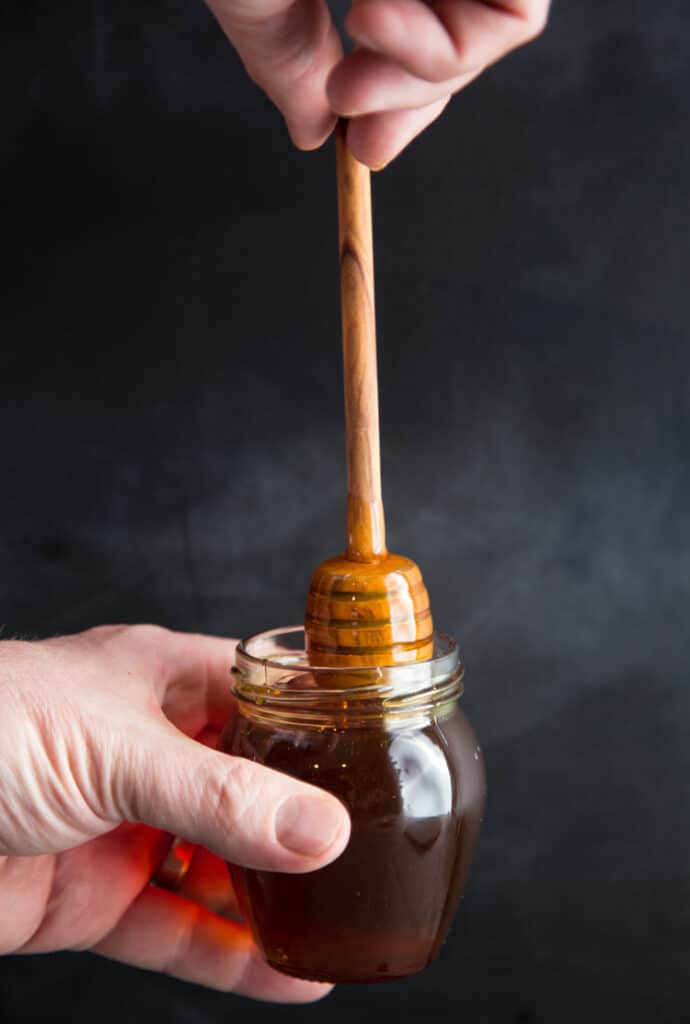 Smoked Honey in a small glass jar with a wooden honey stick dipped in.
