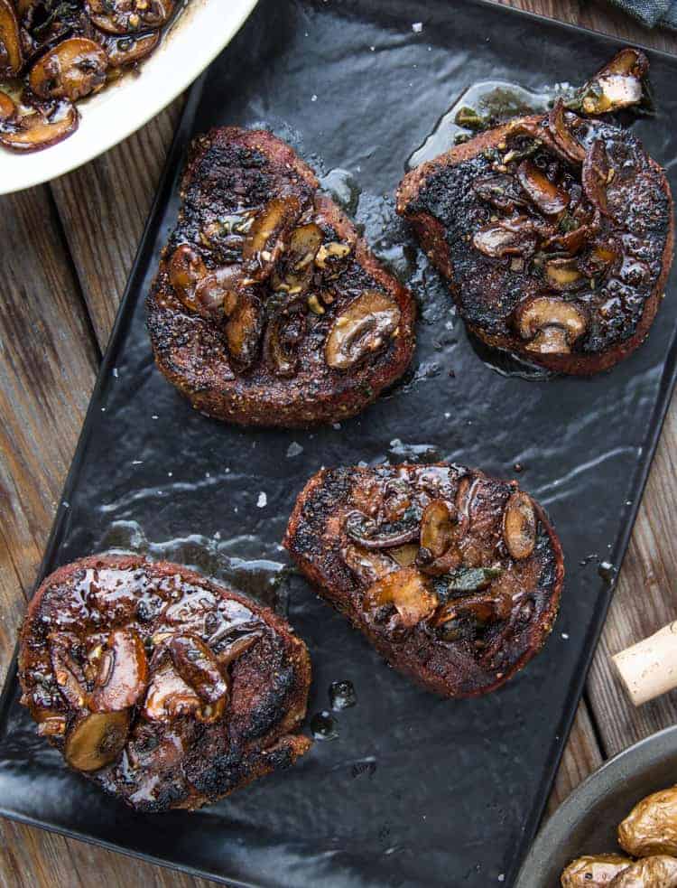 Four filet mignon steaks topped with a mushroom and brown butter sauce. 