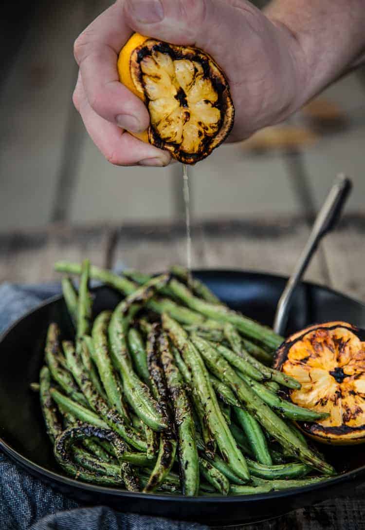 Grilled lemon half being squeezed onto grilled green beans