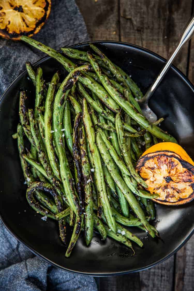 Grilled Green Beans on a black plate with grilled lemon to the side