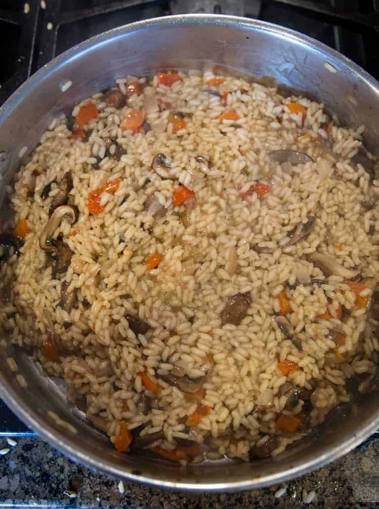 risotto cooking in a skillet with broth, mushrooms and peppers.