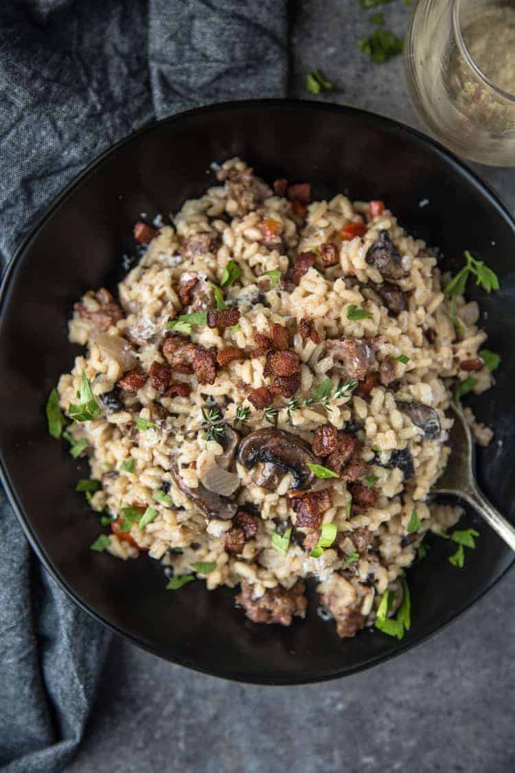A bowl of Smoked Sausage and Mushroom Risotto with a glass of wine.