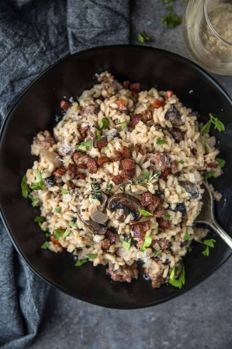 A bowl of Smoked Sausage and Mushroom Risotto with a glass of wine. 