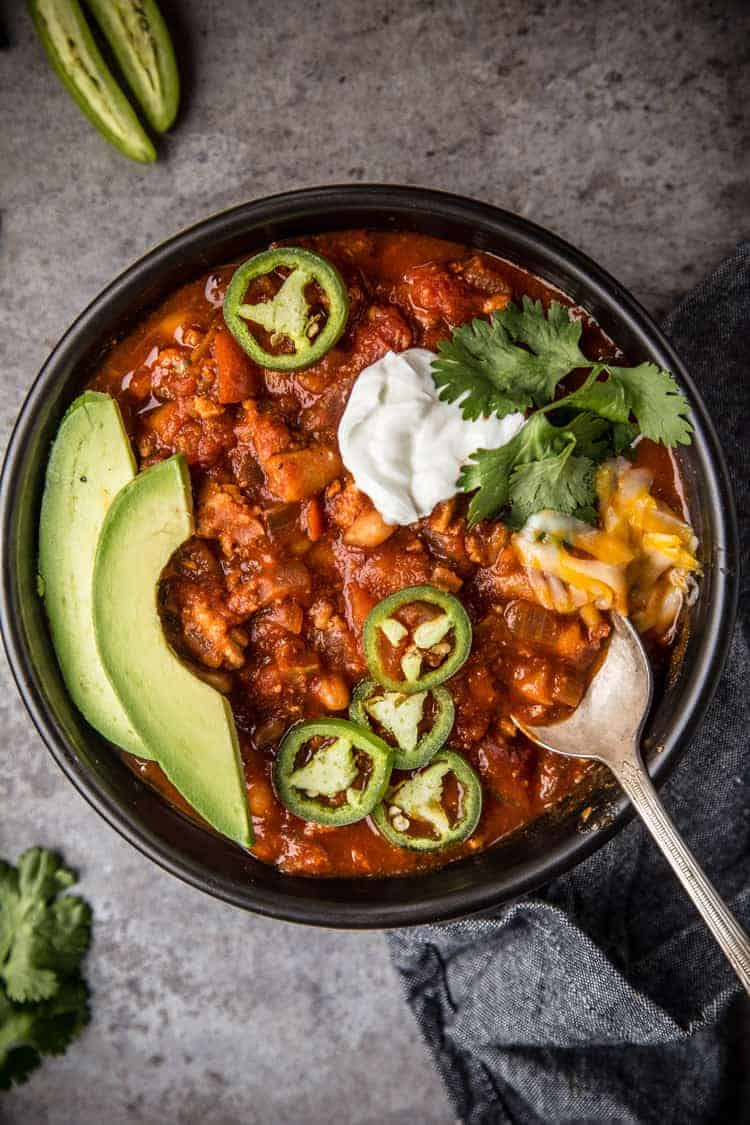 A bowl of Turkey Chili with avocado and sour cream with a spoon in it