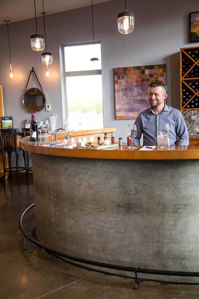 man smiling behind a wine bar