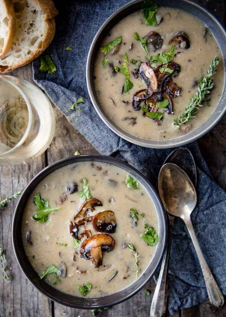Two bowls of wild mushroom soup with crusty bread and a glass of wine