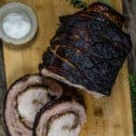 Grilled Porchetta Roast on a cutting board with slices cut showing the filling