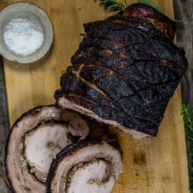 Grilled Porchetta Roast on a cutting board with slices cut showing the filling