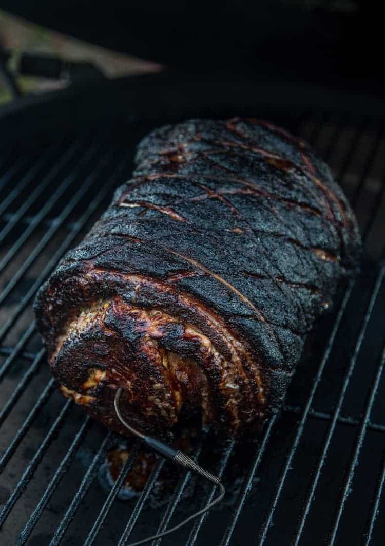 Porchetta roast on a grill with a thermometer in the end.