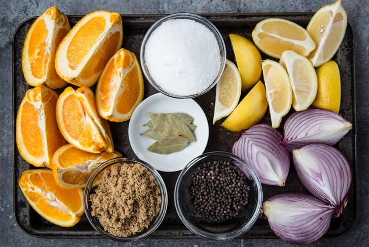 Ingredients on a tray: orange, lemon, red onion, bay leaf, sugar, peppercorns, salt.