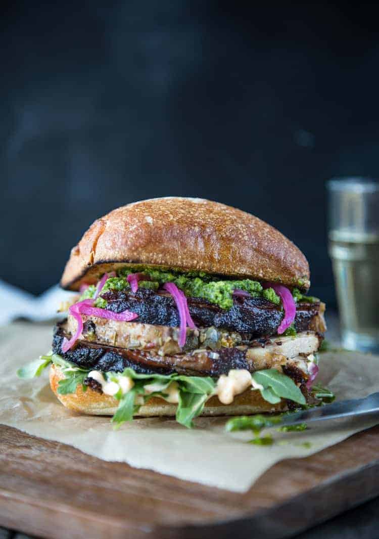 Porchetta Sandwich with pickled onions, aioli, and jalapeño chimichurri sauce on a cutting board.