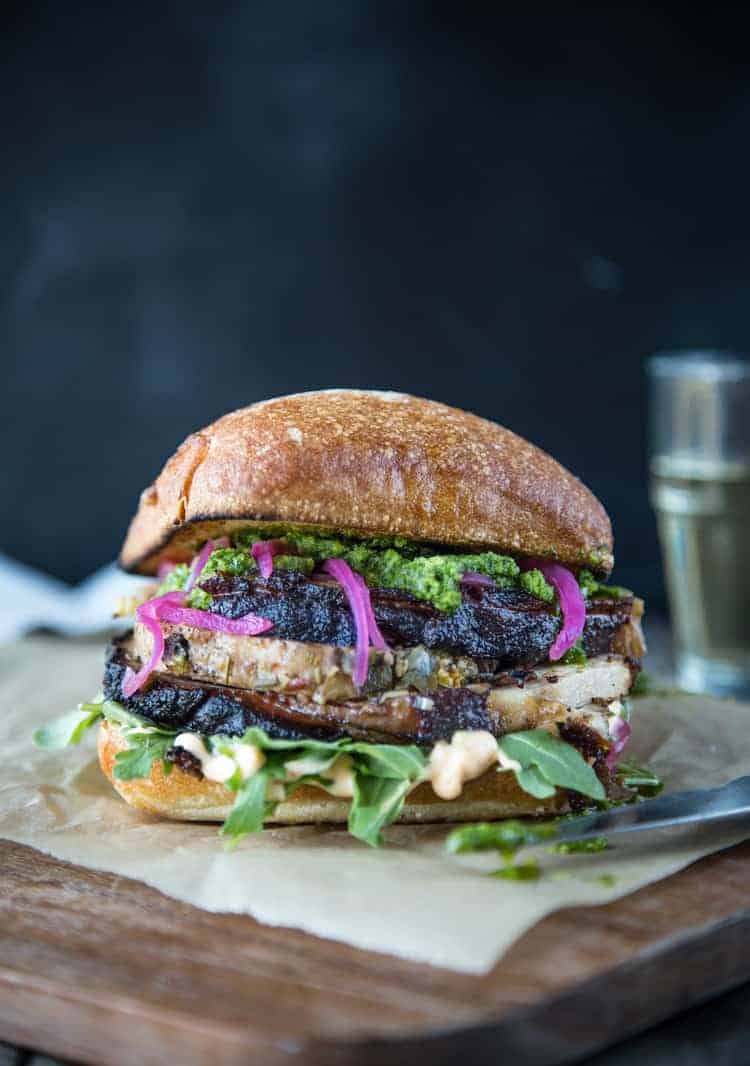 Porchetta Sandwich with pickled onions, aioli, and jalapeño  chimichurri sauce on a cutting board. 