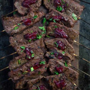 Beef skewers on a cutting board with cranberry relish.