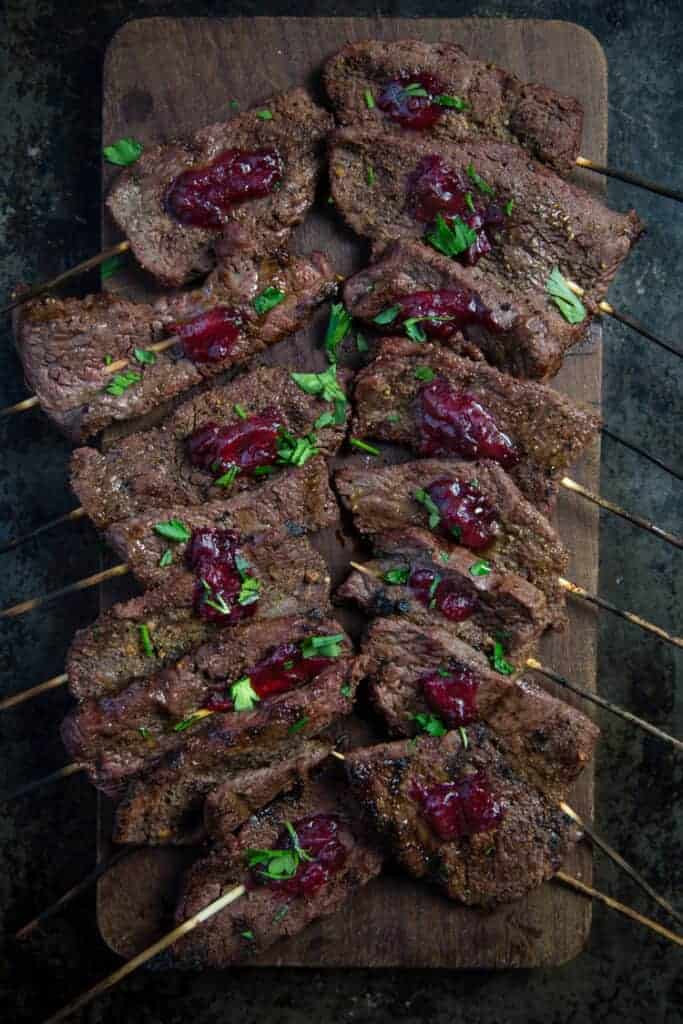 Wine marinated grilled beef skewers with cranberry sauce on a cutting board