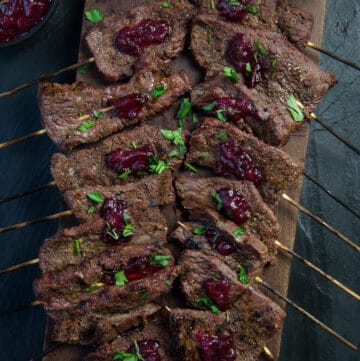 Steak skewers on a cutting board with cranberry relish.