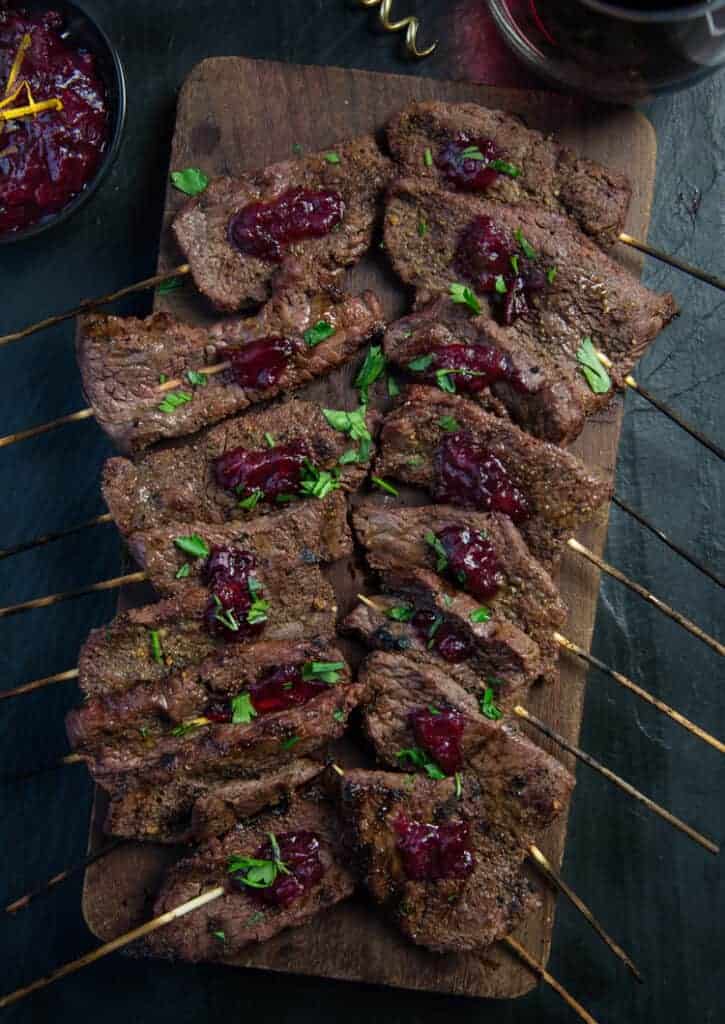 Grilled Beef skewers on a cutting board topped with cranberry sauce