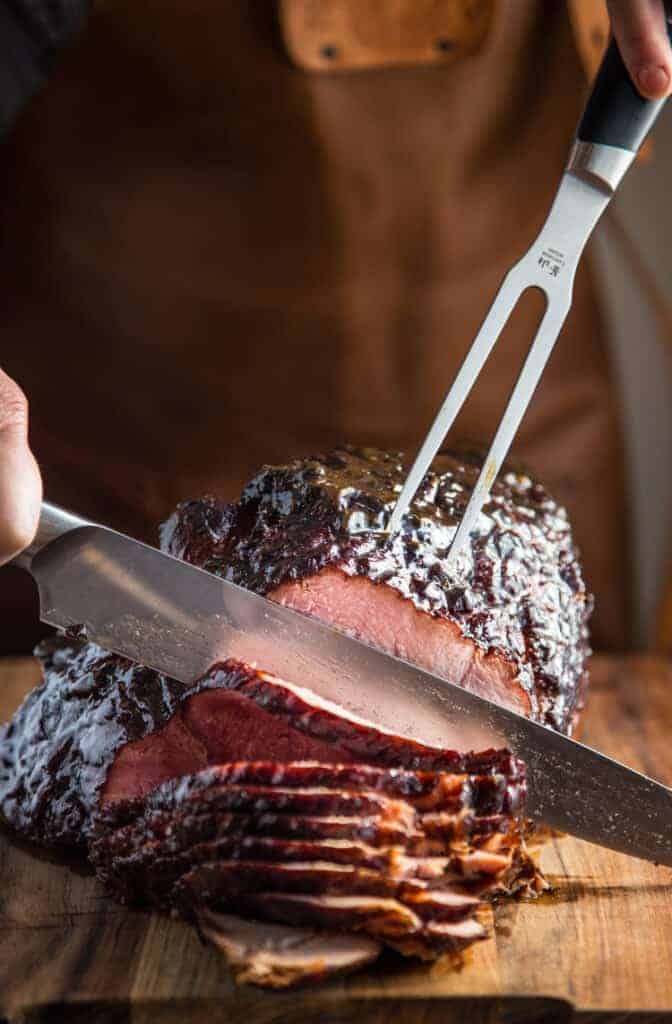 Slicing smoked ham after the brown sugar glaze has set.