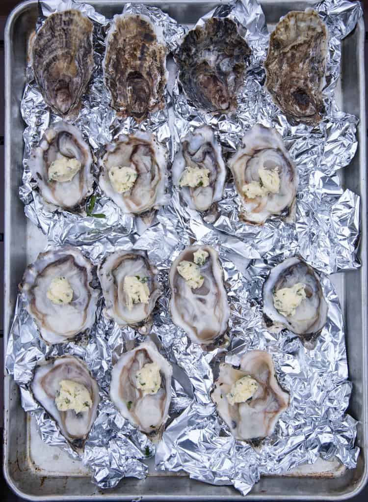 A baking sheet of open oysters topped with a white wine butter, ready for the grill